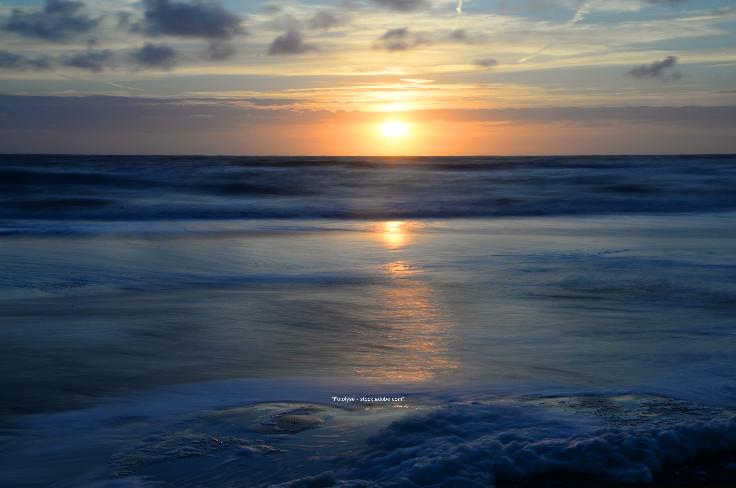 Foto vorne tief dunkel blaues Meer und darüber die dunkel gelbe Sonne welche am Horizont im Meer versinkt