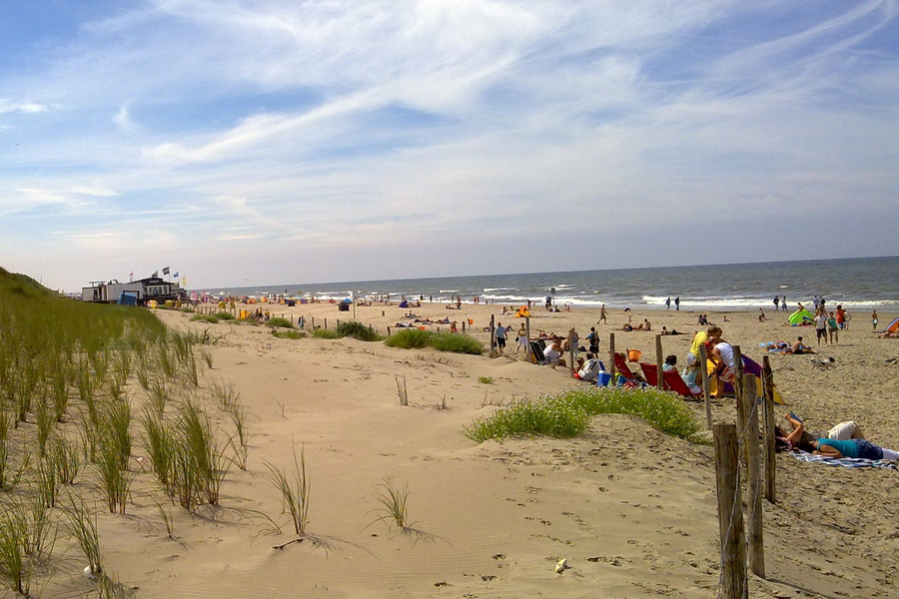 Foto mit Düne, Strand und Meer, darüber blauer Himmel mit weißen Wolken